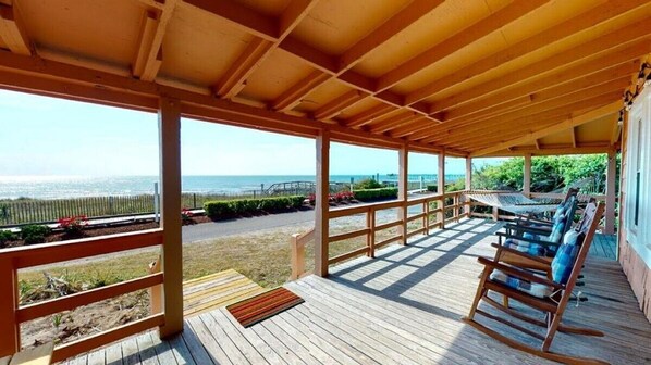 A wooden deck with a view of the ocean, a covered seating area, and a pathway leading to the beach.