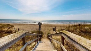 A wooden boardwalk leading to a beach with a clear view of the ocean.