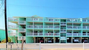 A multi-story hotel with balconies on each floor, a white picket fence in front, and a clear blue sky.