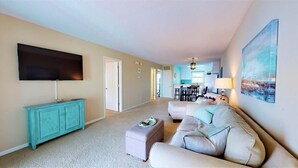 A living room with a sofa, ottoman, and a flat-screen TV mounted on the wall.