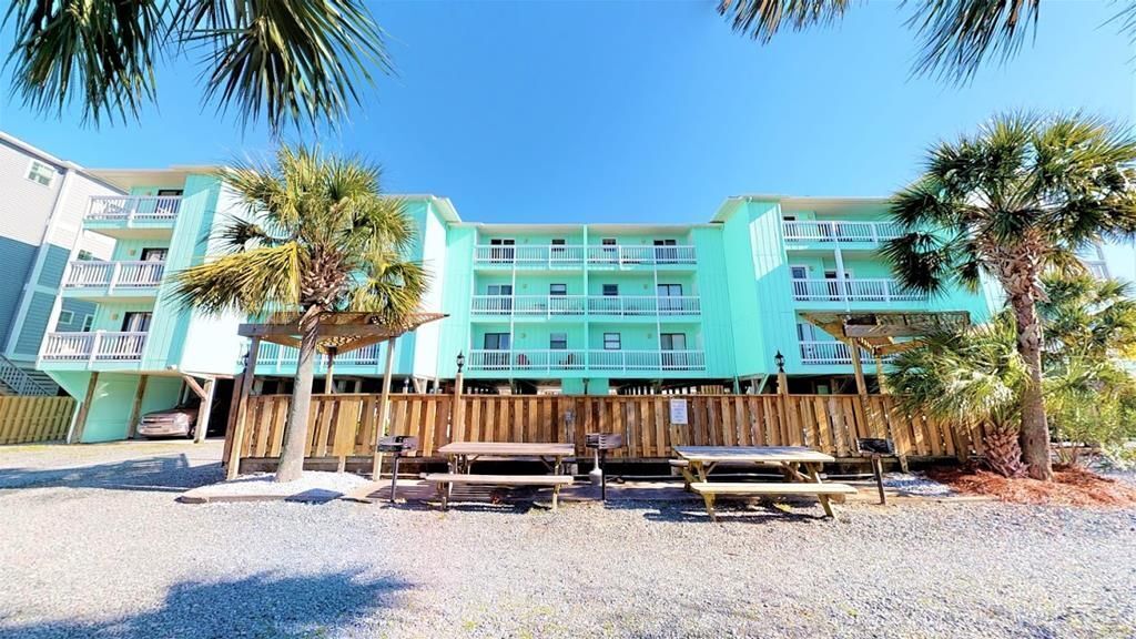 A multi-story hotel with a light blue exterior, balconies, and palm trees in the foreground.