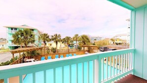 A balcony with a view of a pool and palm trees, wooden deck chairs, and a turquoise railing.