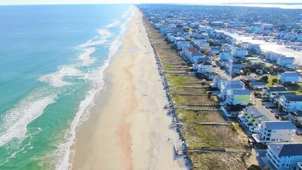 An aerial view of a coastal residential area with houses along the beach and a clear view of the ocean.