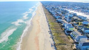 An aerial view of a coastal residential area with houses along the beach and a clear view of the ocean.