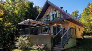 A two-story log cabin with a balcony and a covered porch. - Lee's Lakeside Lair - Three Bedroom Cottage, Sleeps 6 (Commanda)