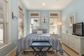 Un dormitorio con cama, cómoda, televisor y ventana con persianas.