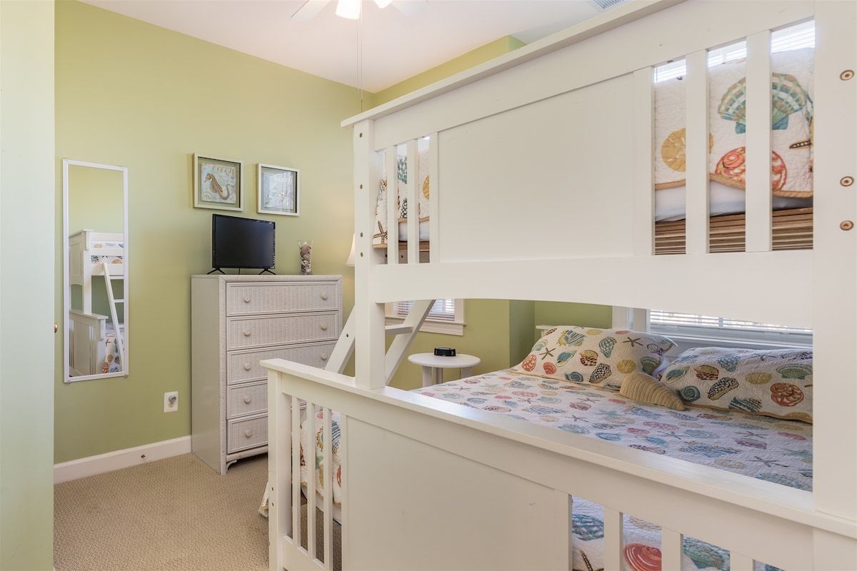 Habitación infantil con literas, cómoda, televisor y ventana con persianas.