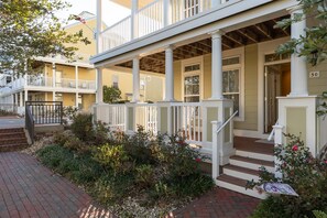 A two-story building with a porch, white railings, and a brick pathway.