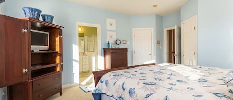 Ein Schlafzimmer mit Bett, Holzmöbeln, Deckenventilator und Blick auf einen Flur.