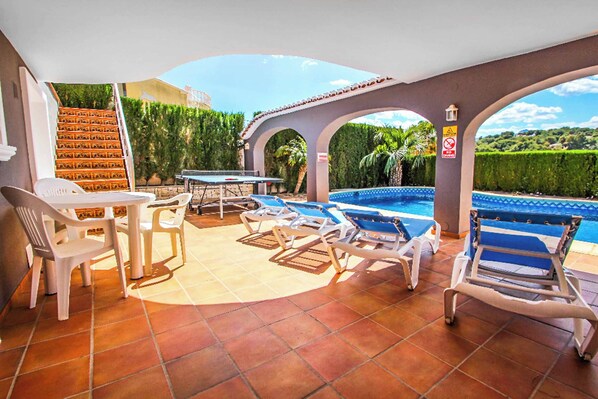A poolside area with lounge chairs, a table, and a staircase leading to an upper level. - Villa Mi Sueno Dos (Benissa)