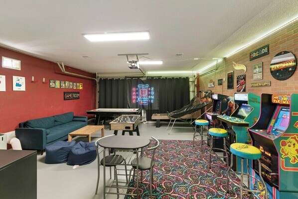 A room with a sofa, a table, chairs, a foosball table, and arcade games. - Chandler Hideaway - Relax & Unwind ,Heated pool (Chandler)