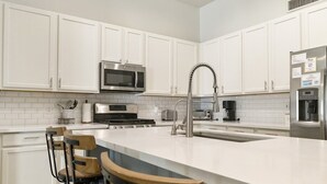 A modern kitchen with white cabinetry, a central island with bar stools, stainless steel appliances, and recessed ceiling lighting. - Chandler Hideaway - Relax & Unwind | Heated pool (Chandler)