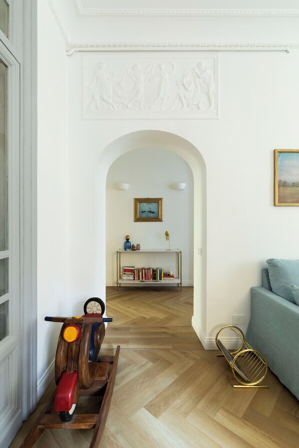 A hallway with a wooden floor, a white wall with a decorative molding, a framed picture, and a bookshelf. - Belle Epoque House of Mirror (Rome)