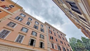 Un immeuble à plusieurs étages, doté d’une façade beige, de nombreuses fenêtres avec volets et d’une base en pierre.