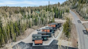 A row of modern cabins with a "UNPLUG" sign, surrounded by a forested area with a road curving around. - Tiny Cabin Getaway #6 @Unplug Resort, Sauna, Full Kitchen (Brian Head)