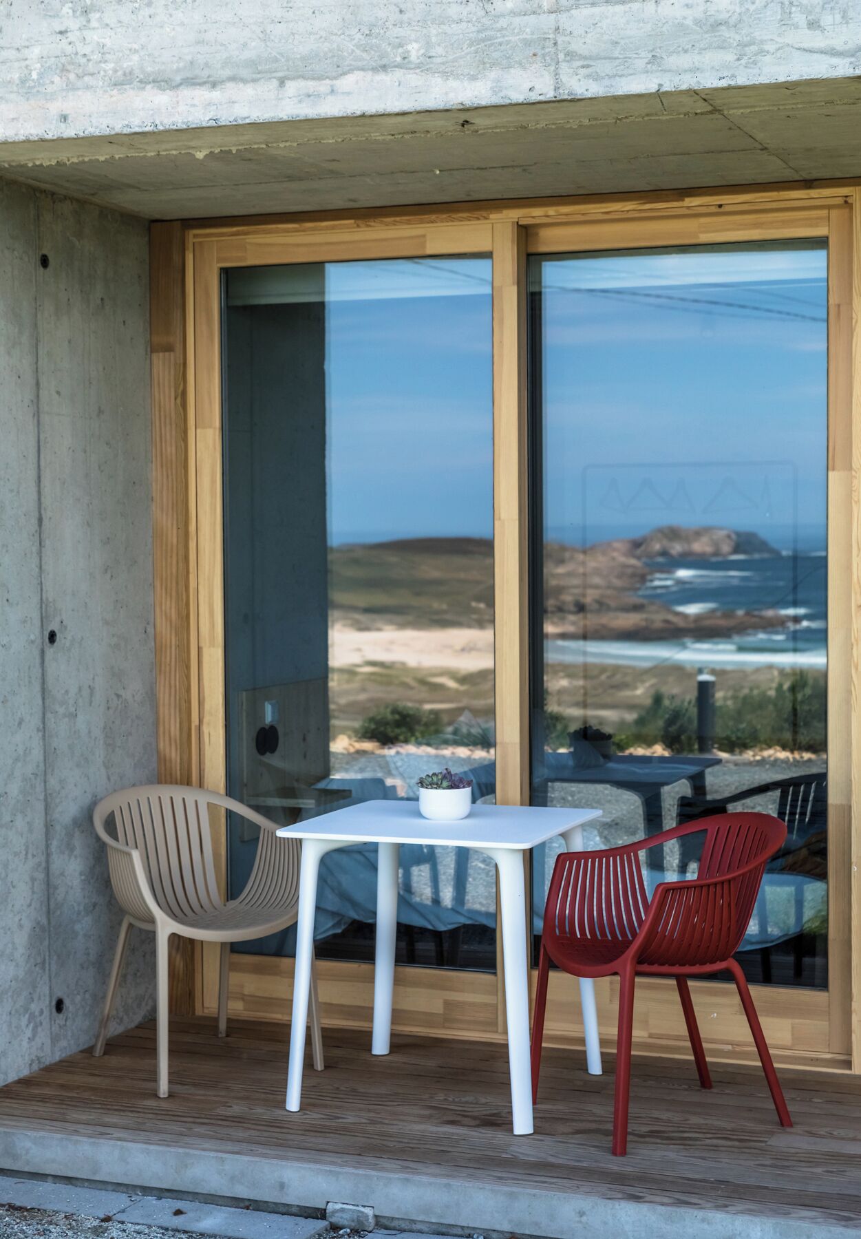 Un pequeño espacio al aire libre con dos sillas y una mesa, con vistas a un paisaje pintoresco a través de amplios ventanales.