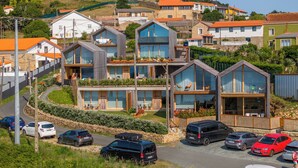 A residential area with modern houses featuring large windows and balconies, surrounded by greenery and a winding road. - Doniños Nature (Ferrol)