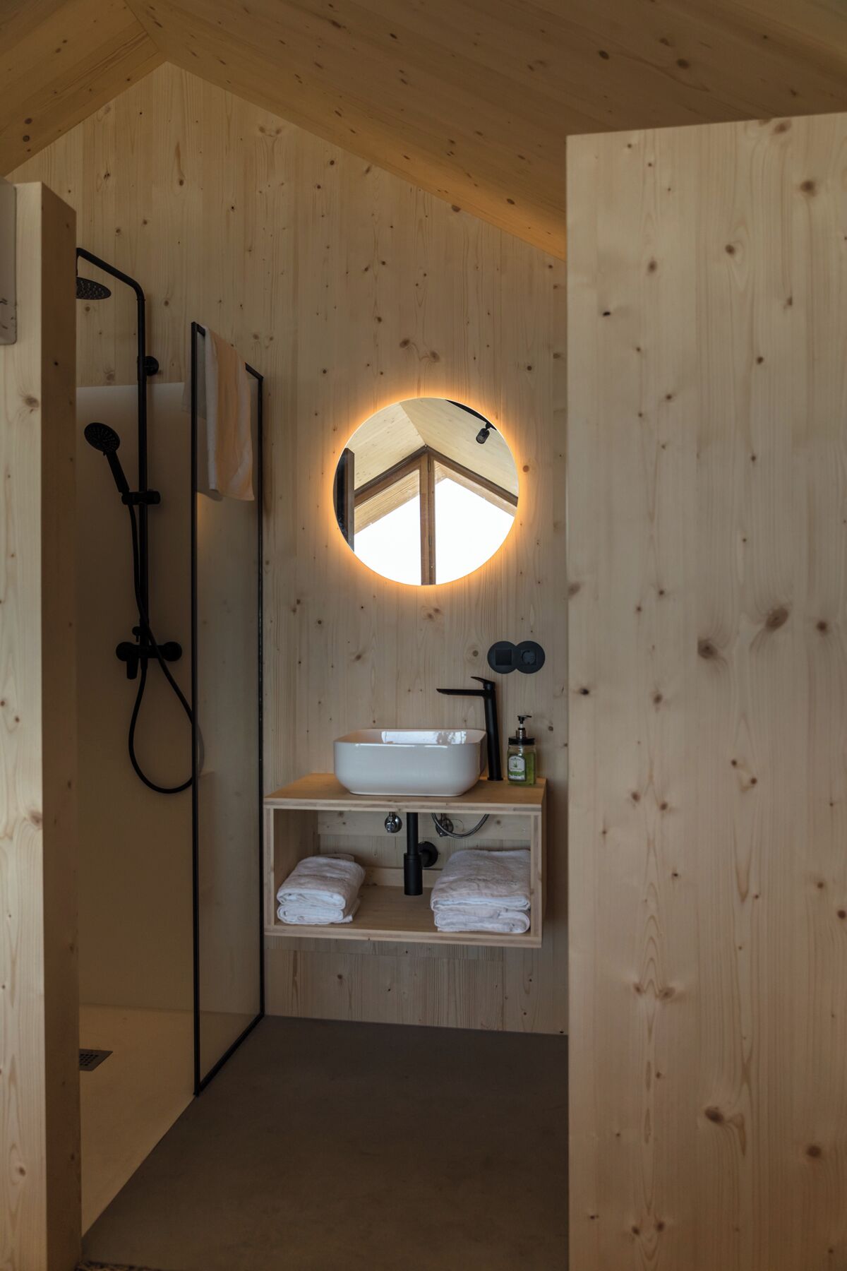 Un bagno in legno con uno specchio rotondo, un lavabo bianco e una doccia.