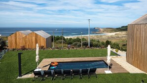 A pool area with a view of the ocean, surrounded by wooden structures and a grassy lawn. - Doniños Nature (Ferrol)