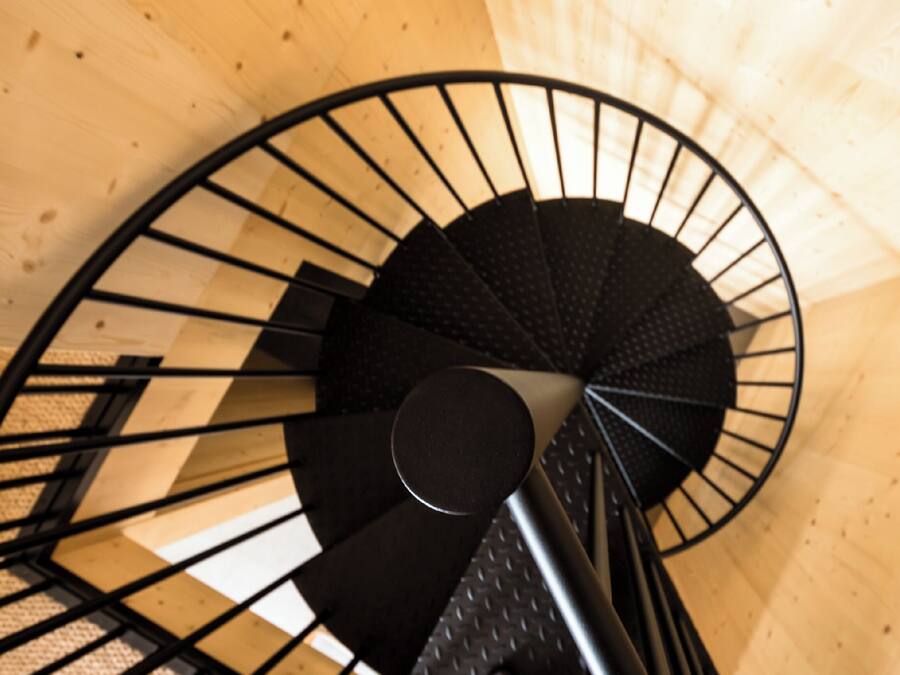 Un escalier en colimaçon avec une rampe noire et des marches en bois.