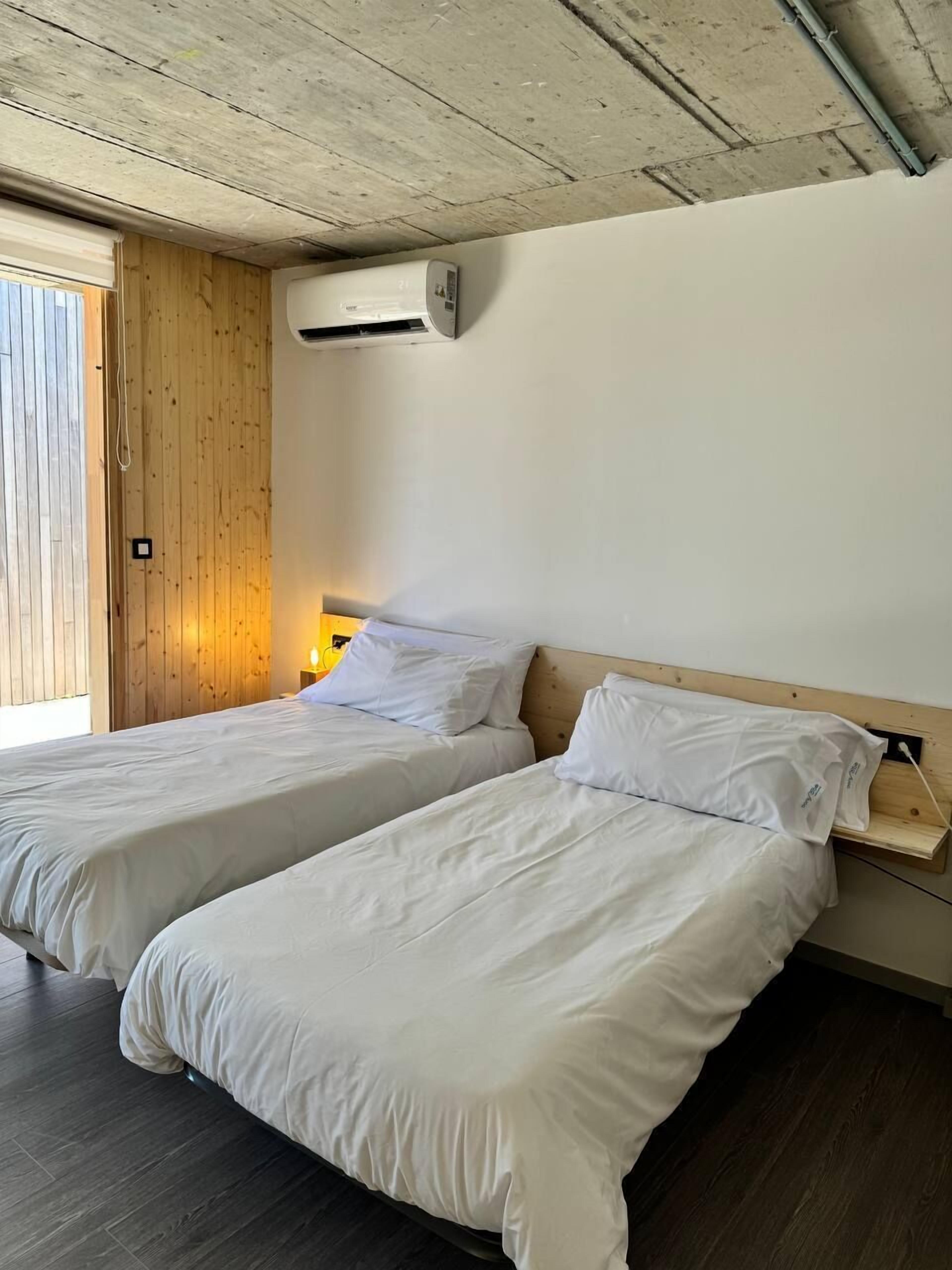 Ein Zimmer mit zwei Betten, Holzwänden und einer Decke mit freiliegenden Balken. Eine Klimaanlage ist ebenfalls vorhanden.