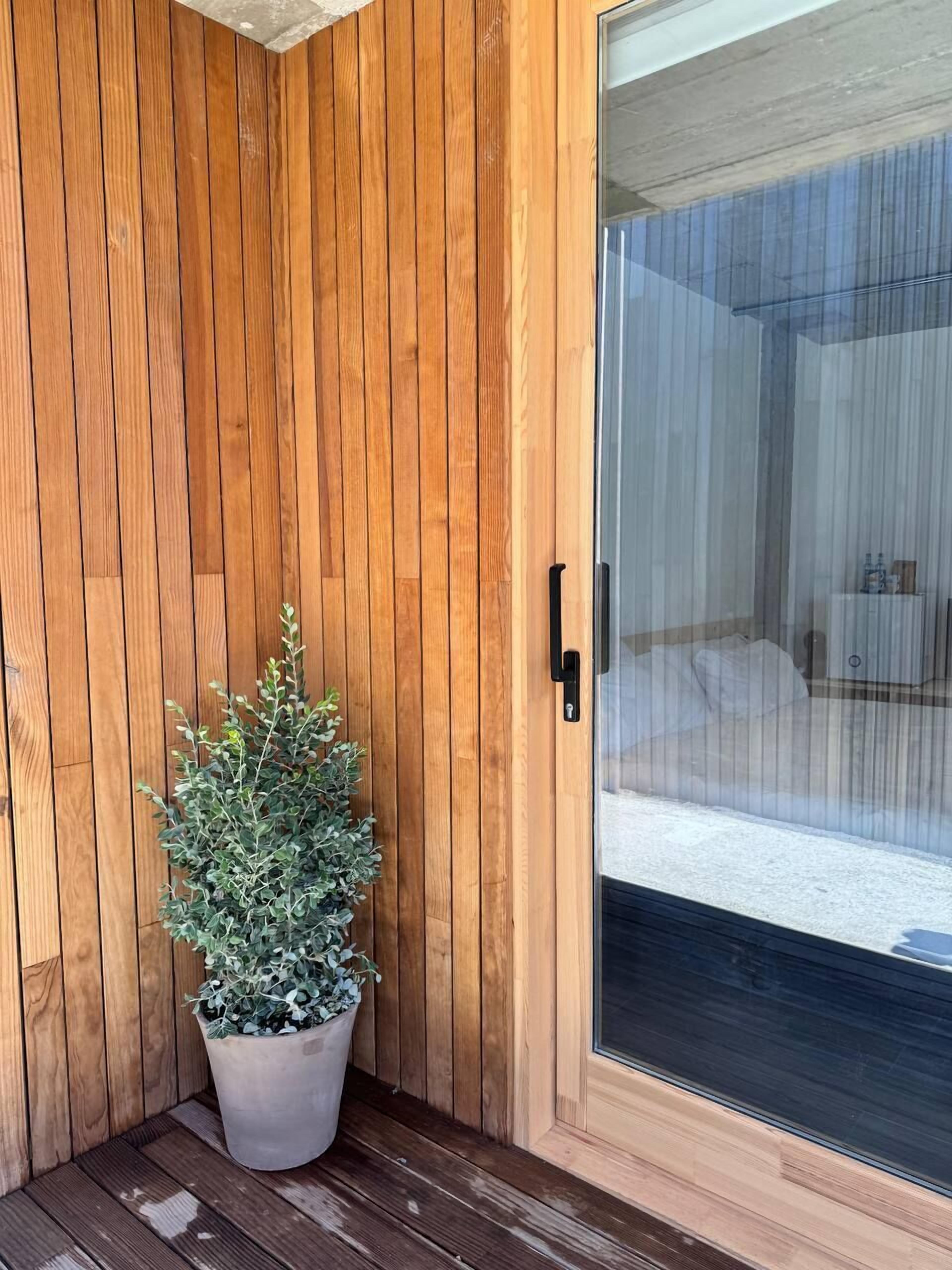 Pared exterior de madera con una planta en maceta, un cristal y un picaporte de metal.