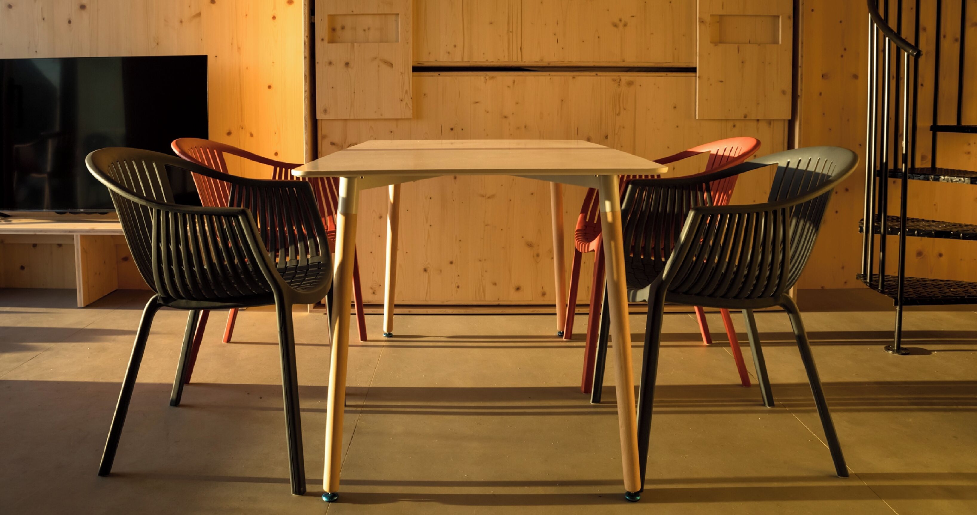 A dining area with a table and four chairs, a wooden wall, and a television in the background.