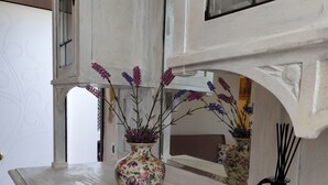 Un meuble blanc, orné de motifs décoratifs, sur lequel sont posés un vase à fleurs et un diffuseur de parfum à bâtonnets.