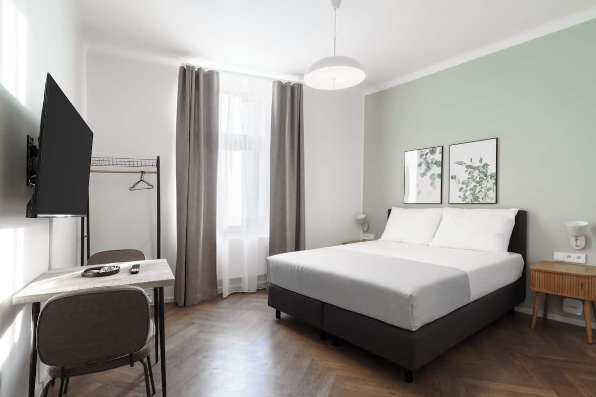 Quarto de hotel moderno com uma cama, uma escrivaninha, uma cadeira, uma TV e duas imagens emolduradas na parede.