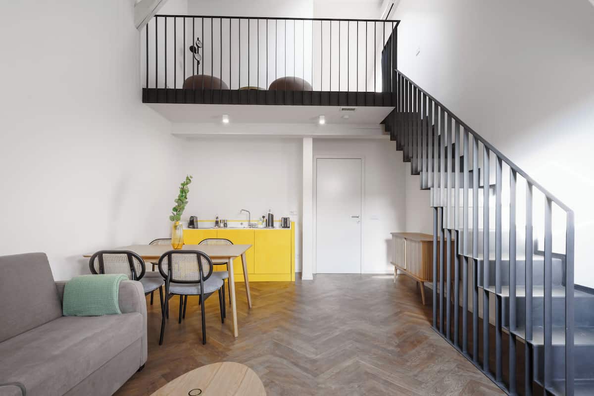 Um interior moderno com área de refeições, sofá, escada e cozinha.