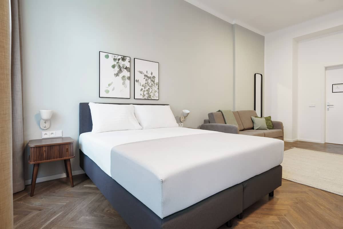 Quarto moderno com uma cama grande, uma mesa lateral, um sofá e duas luminárias fixadas na parede.
