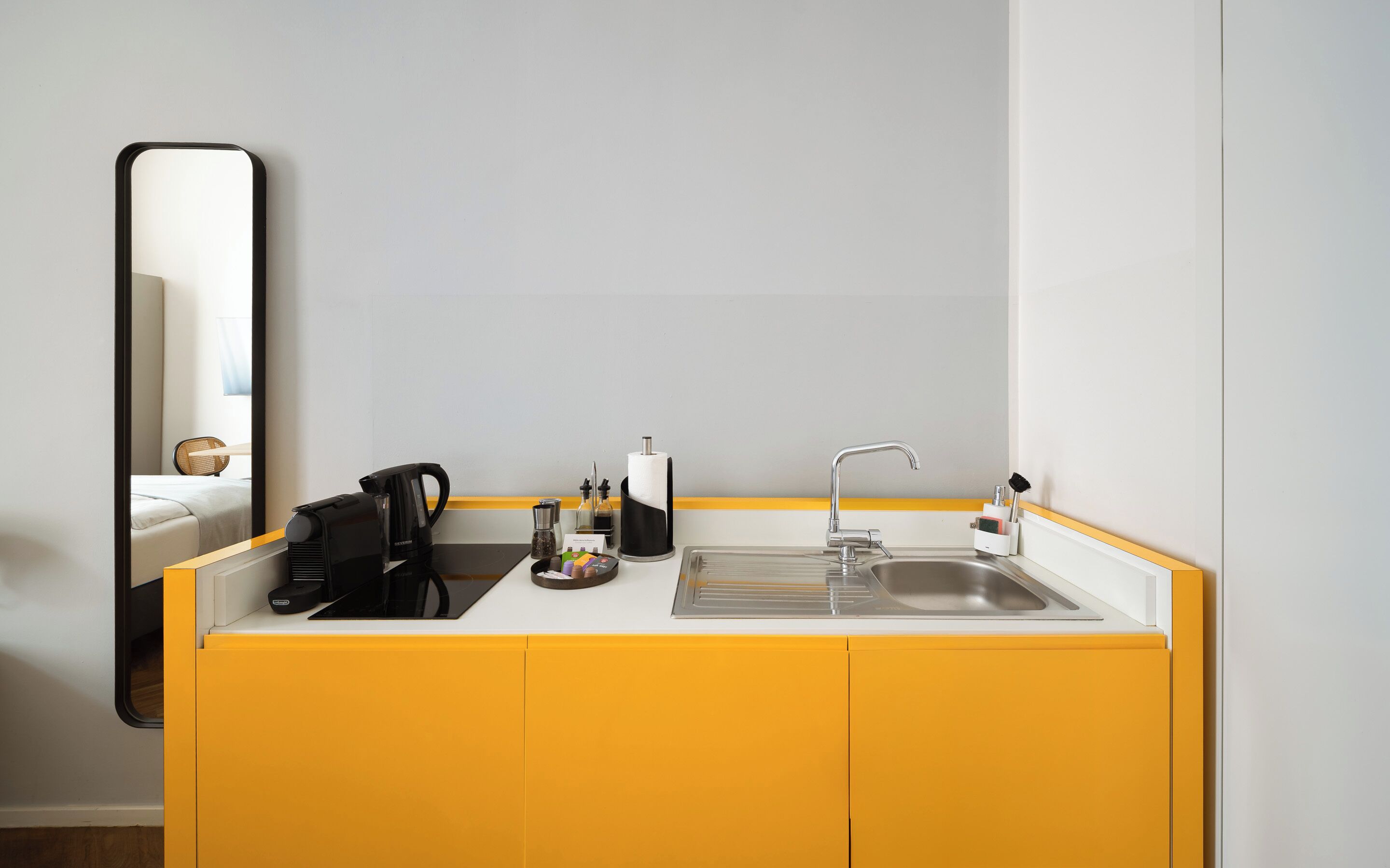 A modern kitchen with a sink, a coffee maker, and a mirror.