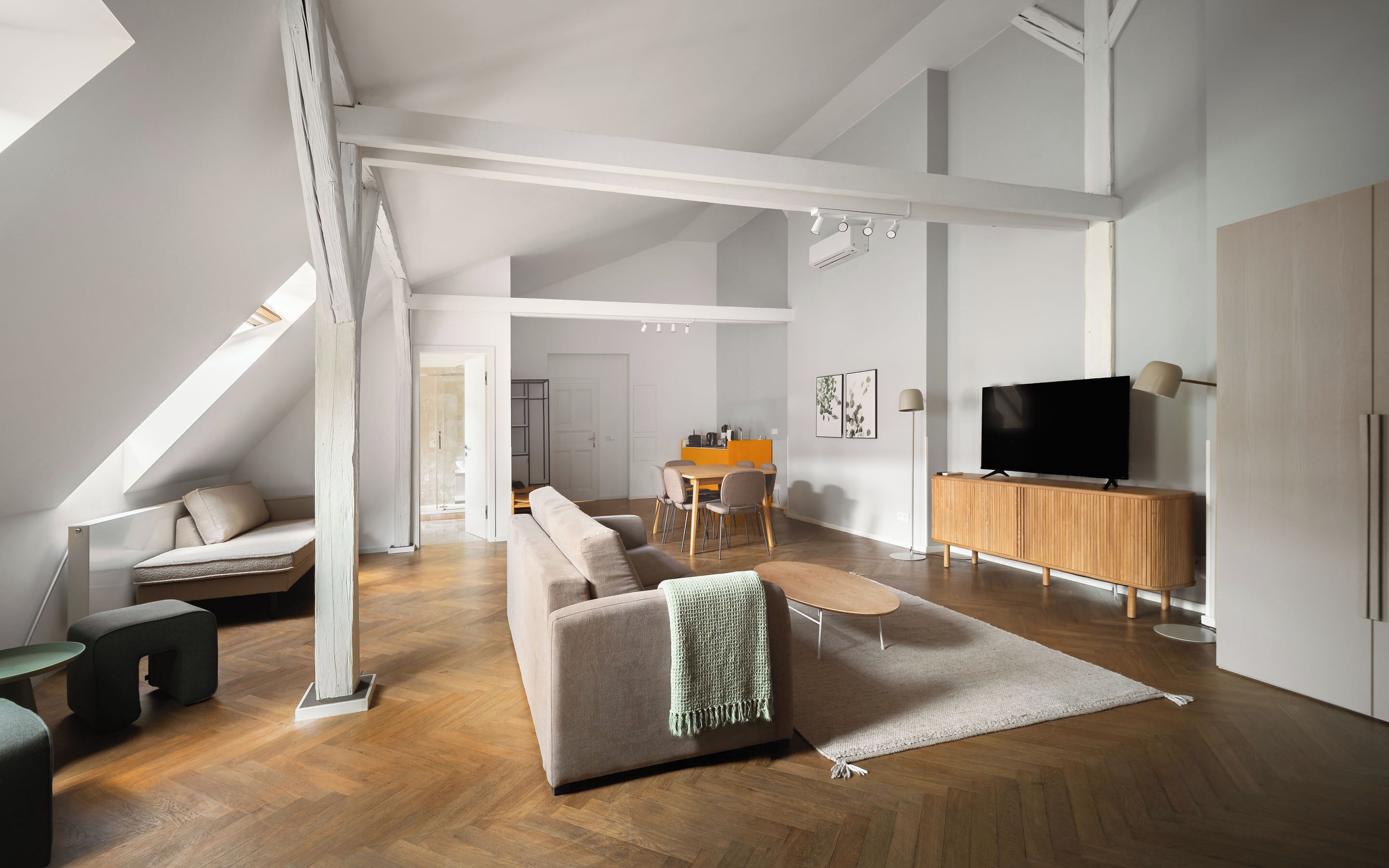 A modern living room with a sofa, a coffee table, a TV on a wooden cabinet, and a dining area with a table and chairs.