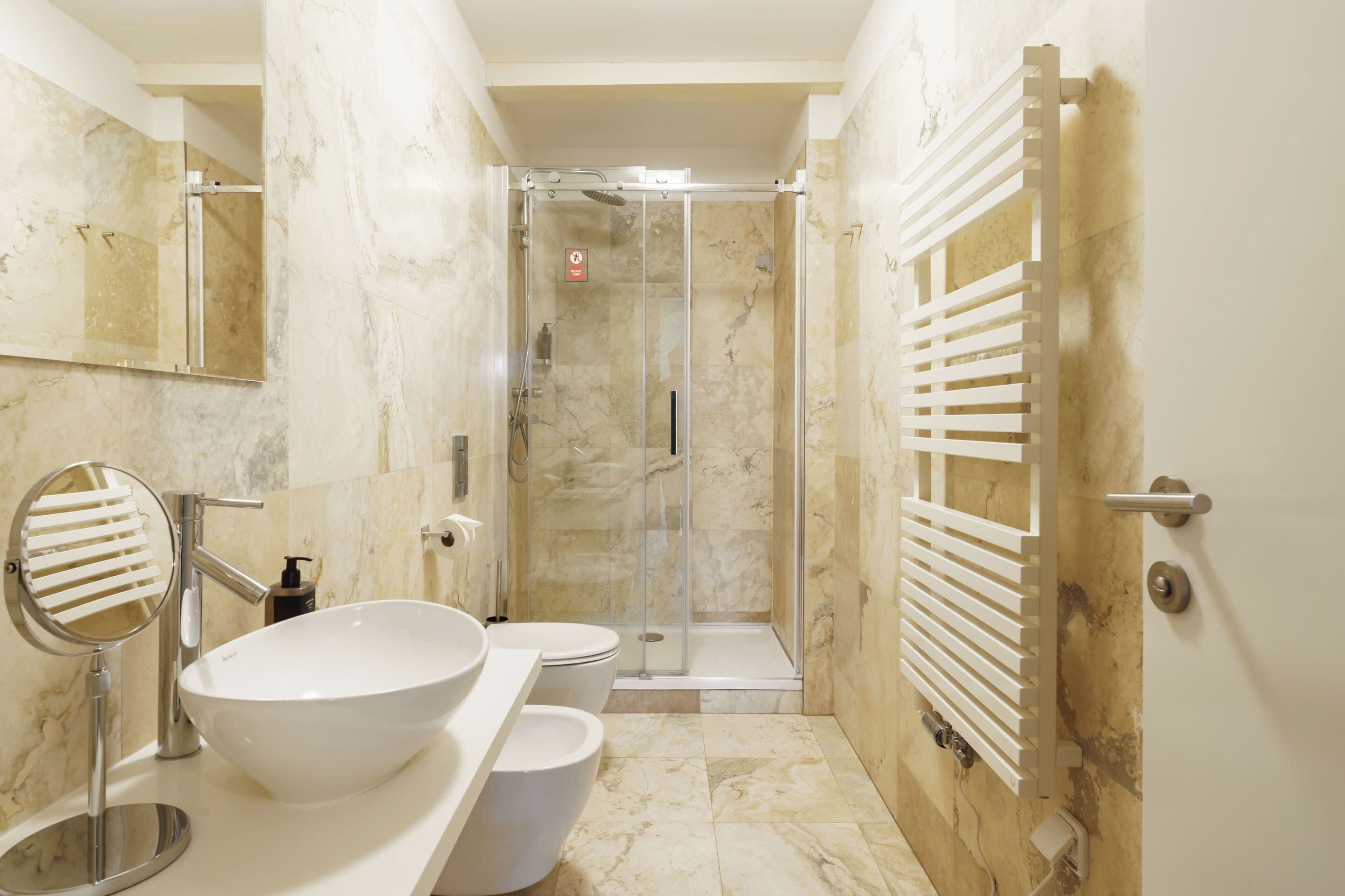 A modern bathroom with a large white sink, a mirror, a toilet, and a shower area.