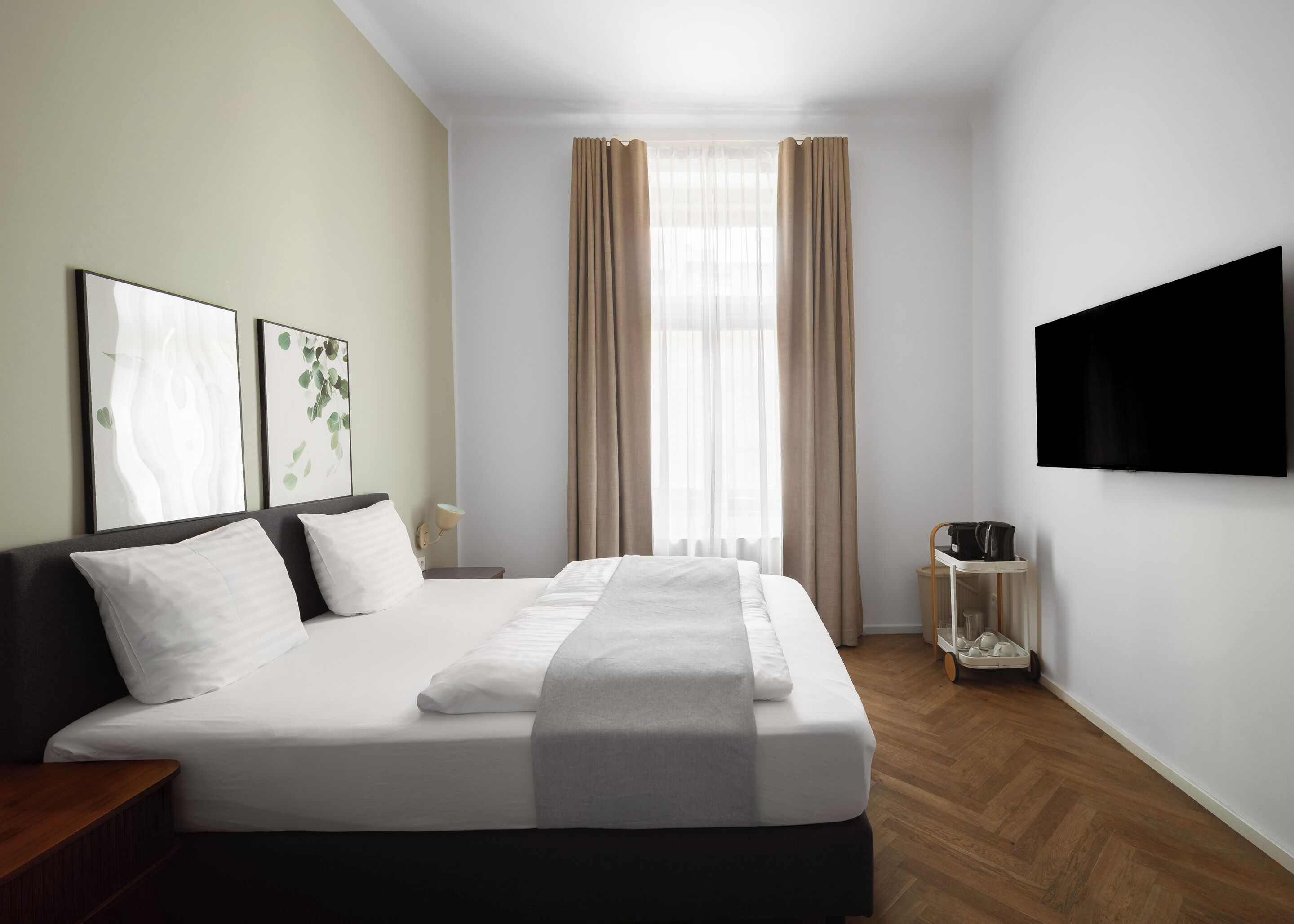 Ein Hotelzimmer mit einem großen Bett, einem Flachbildfernseher, einem Nachttisch und einem Fenster mit Vorhängen.