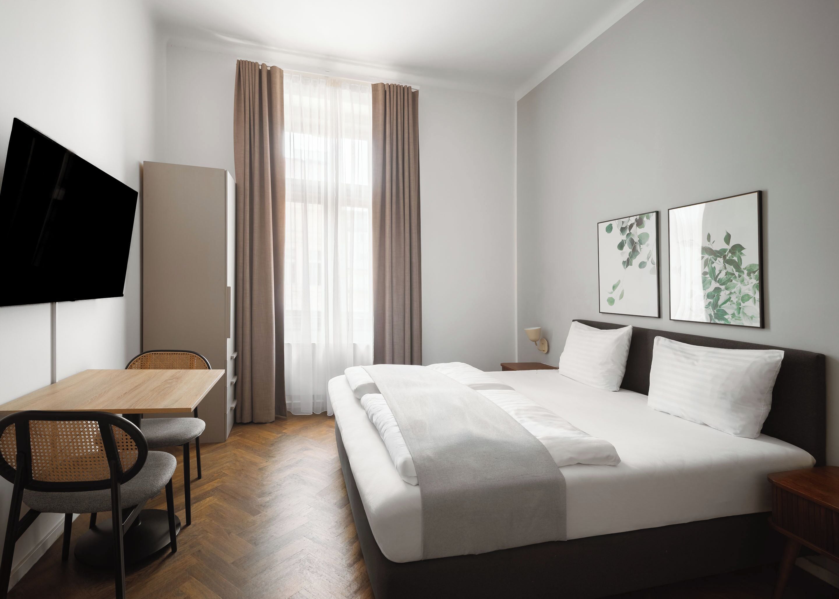 Habitación de hotel con cama, escritorio, silla, televisor y obras de arte en la pared.