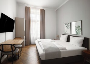 Ett hotellrum med en säng, ett skrivbord, en stol, en tv och konstverk på väggen.