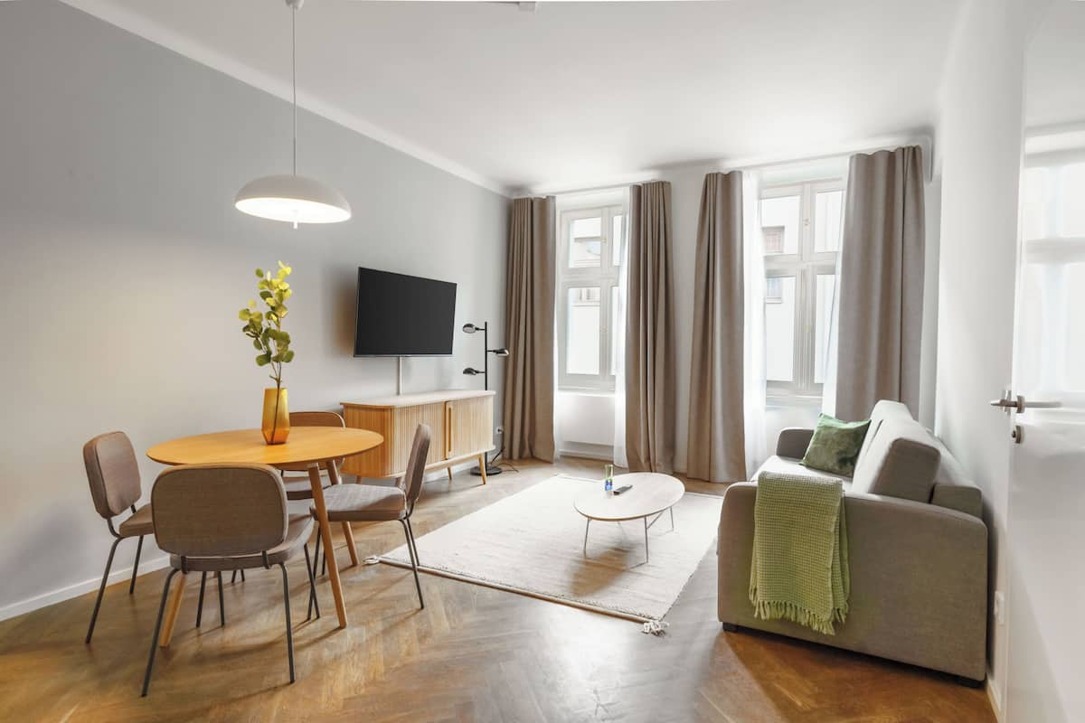 Uma sala de estar moderna com uma mesa de jantar de madeira, cadeiras, um sofá e uma televisão de tela plana fixada na parede.