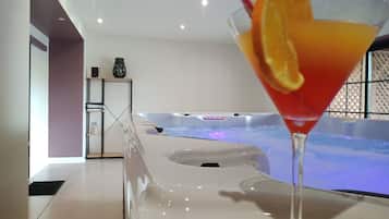 Un interior moderno con una mesa de vidrio, una copa de martini con un adorno de naranja, y un jacuzzi al fondo.