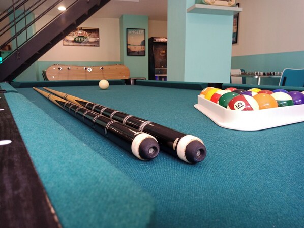 A pool table with a cue stick, billiard balls, and a staircase in the background.