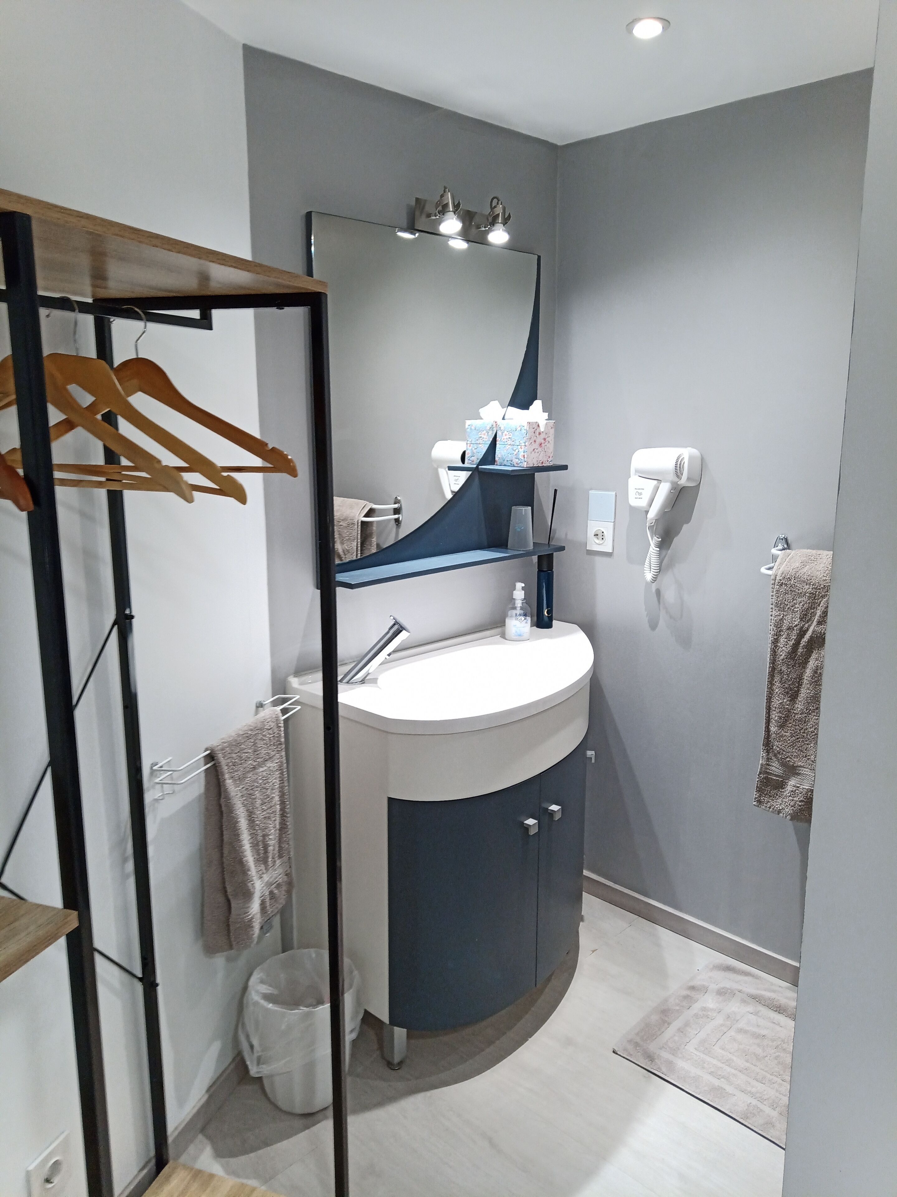 Une salle de bain moderne avec un lavabo incurvé, un miroir, un sèche-cheveux et des cintres en bois.