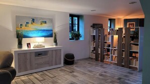 A modern living room with a wooden floor, a white console table with a lamp, a painting, and a bookshelf. - L'Hacienda (Tartas)