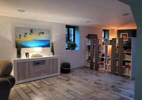 Una sala de estar moderna con piso de madera, una consola blanca con lámpara, un cuadro y una estantería.