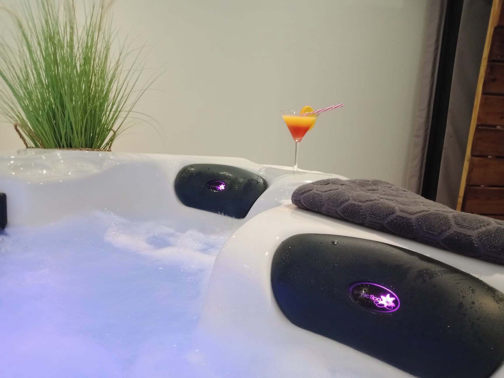 A hot tub with water jets, a glass of orange drink, and a towel.