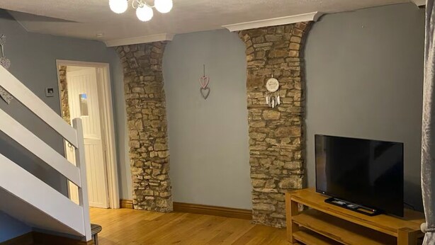 Een woonkamer met een stenen accentmuur, een houten entertainmentmeubel en een trap.