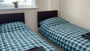 Een kamer met twee bedden, elk voorzien van een geruite sprei, een kleine potplant op de vensterbank en een opgevouwen handdoek op een van de bedden.