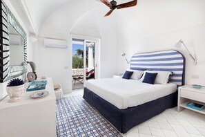 A bedroom with a large bed, a ceiling fan, a bedside table with a lamp, and a view of the outdoors. - Villa Serenity by MyVillaCollection (Anacapri)