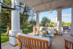 An outdoor patio with a glass-top table, white sofas, and a wooden bench. - Villa Serenity by MyVillaCollection (Anacapri)