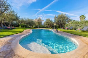 A swimming pool with a tiled deck, surrounded by grass and trees, and equipped with lounge chairs and an umbrella. - Villa Serenity by MyVillaCollection (Anacapri)