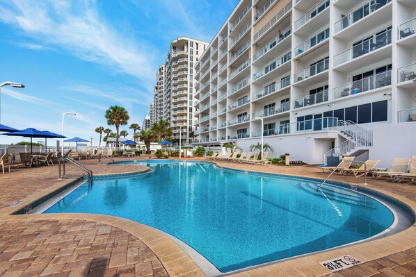 A swimming pool area with lounge chairs and a tall building in the background.